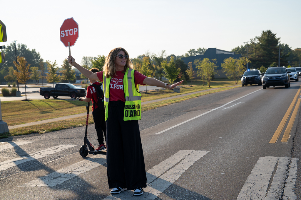 A woman with longe blonde hair holding out a stop sign wearing a neon crossing guard vest 