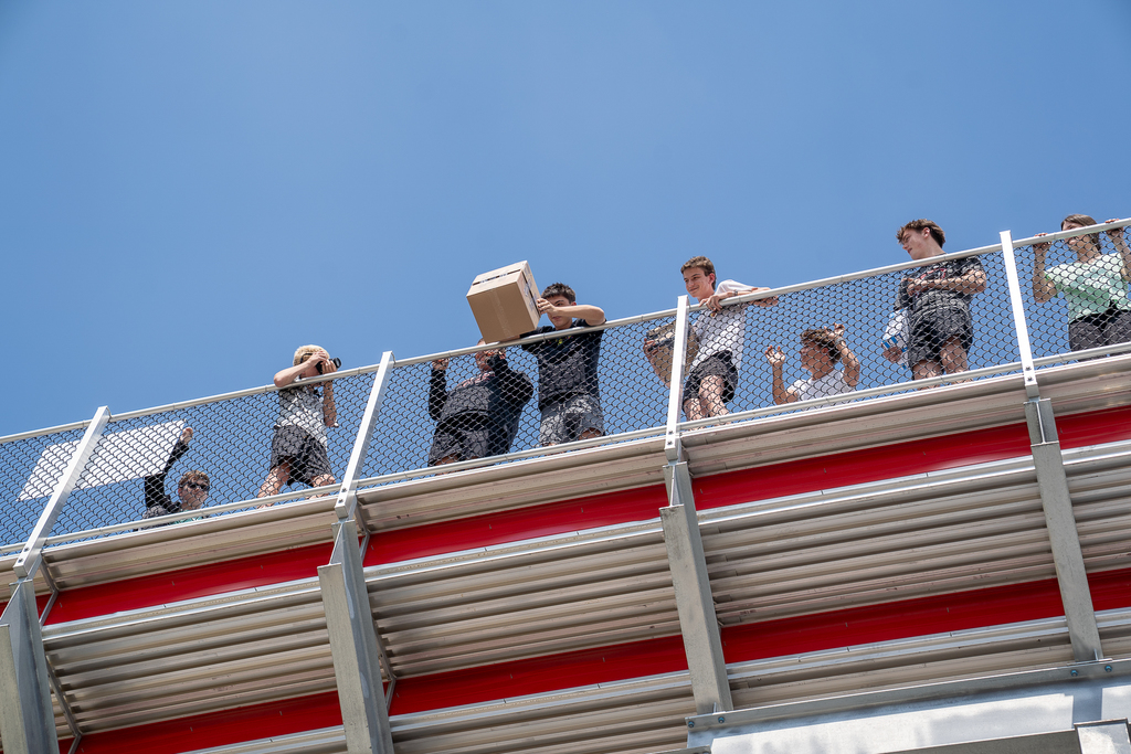 Students high in the bleachers looking down with a box