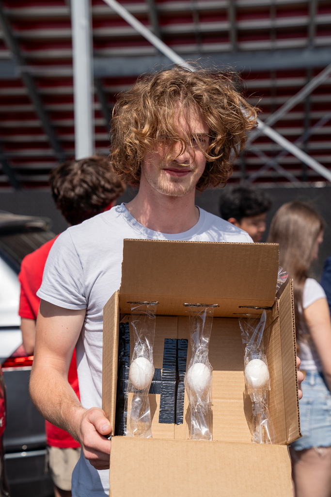 A boy with long hair holding open a box with three taped eggs inside
