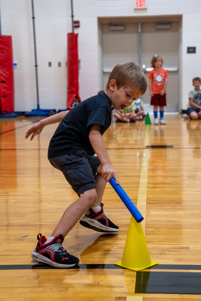 A boy with a blue baton touching a yellow cone