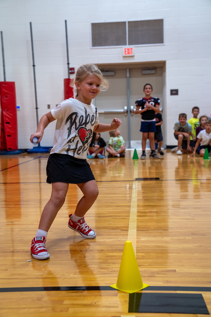 a girl in a white shirt sprinting in the gym with a baton
