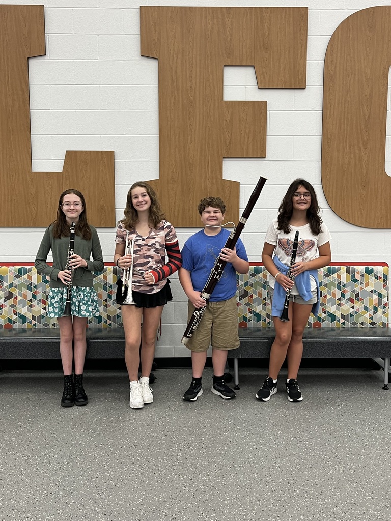4 students (left to right) girl holding oboe, blonde girl holding trumpet,  curly-haired boy holding bassoon, and girl holding oboe