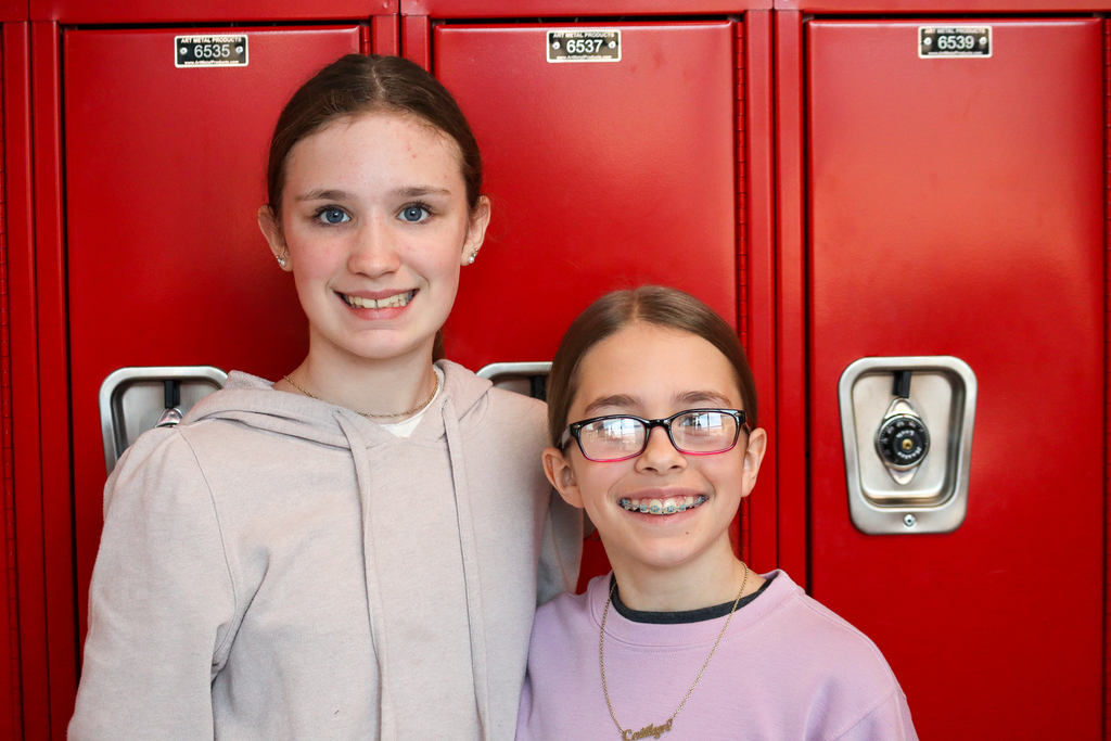 Two girls smiling at the camera in front of red lockers 