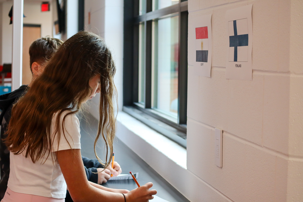 A girl with brown hair writing on paper underneath printed out flags