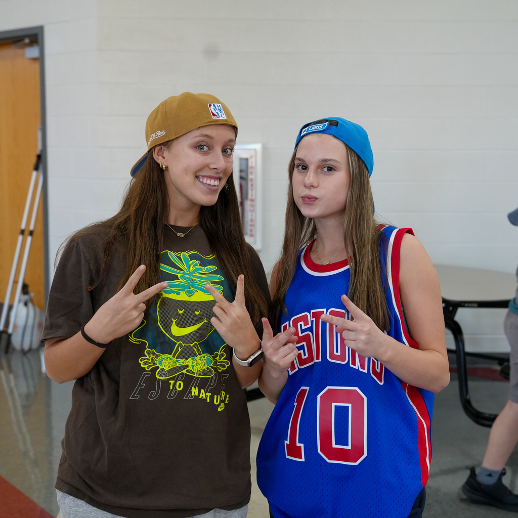Two girls with peace signs with backwards hat and jersey and shorts