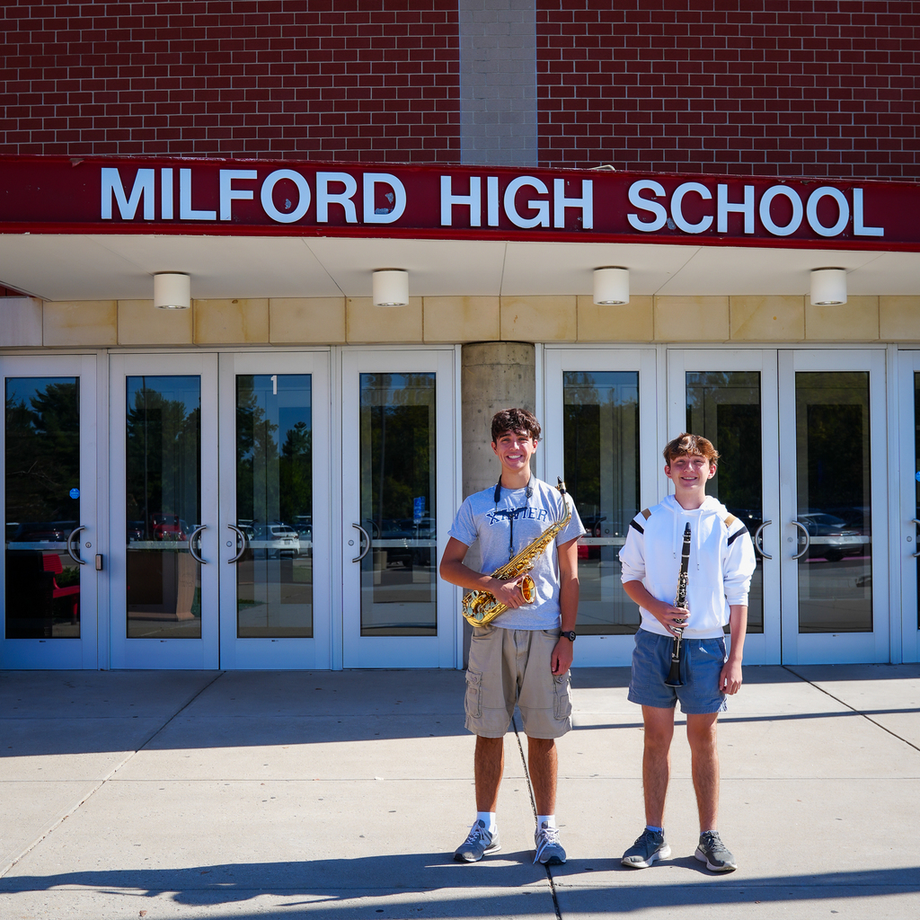 Two students in front of Milford High School holding a saxophone and a clarinet