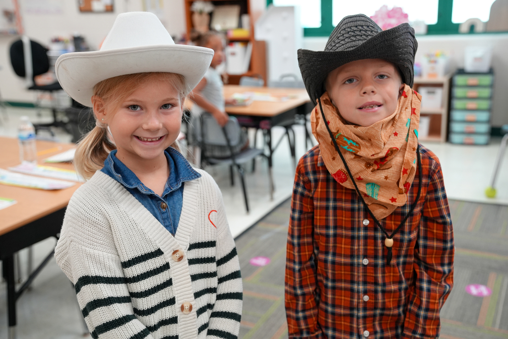 A blonde girl with a jean shirt next to a boy with a cowboy hat and plaid shirt 