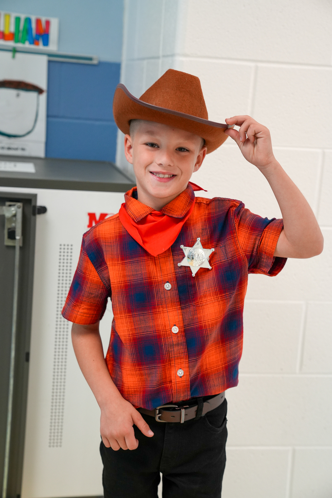 A young boy with blond hair wearing a cowboy hat with a sherrif's badge