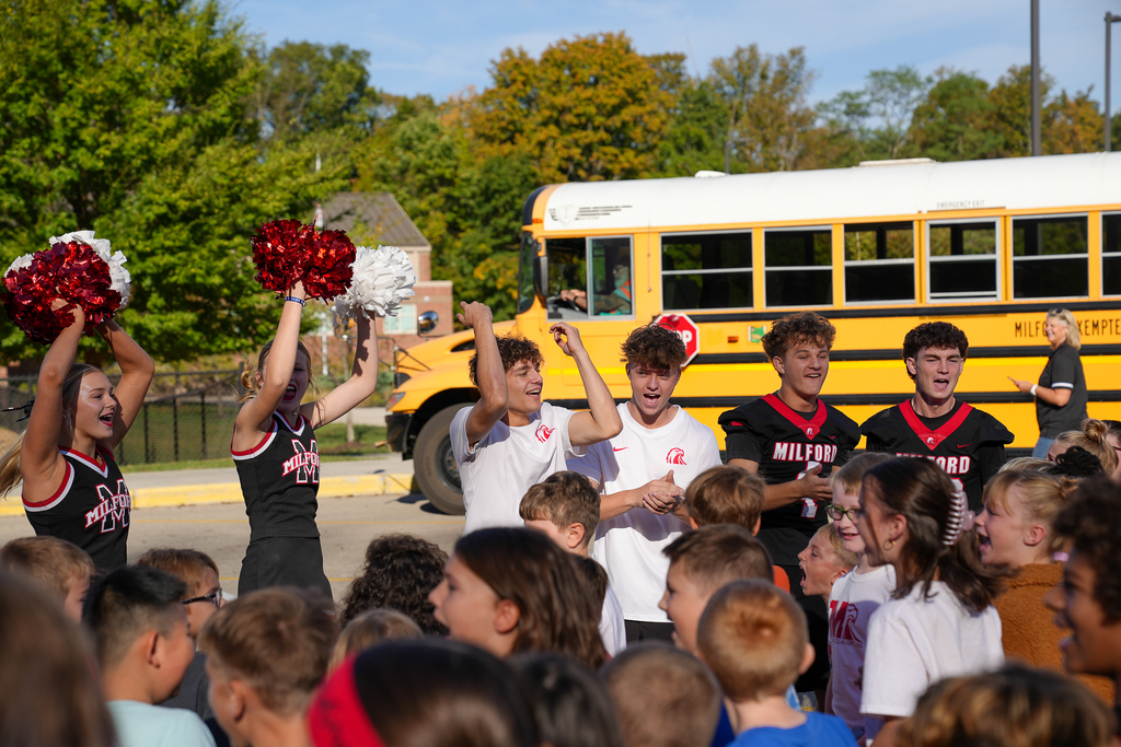 teenage guys in front of a bus cheering to a group of students 