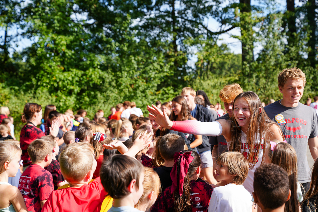 A girl with brown hair reaching over kids to give a high-five