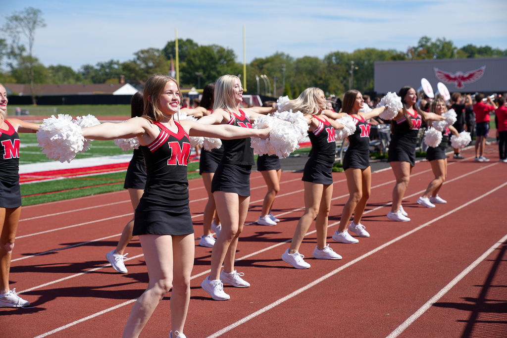 a line of cheerleaders in black outfits with a red M