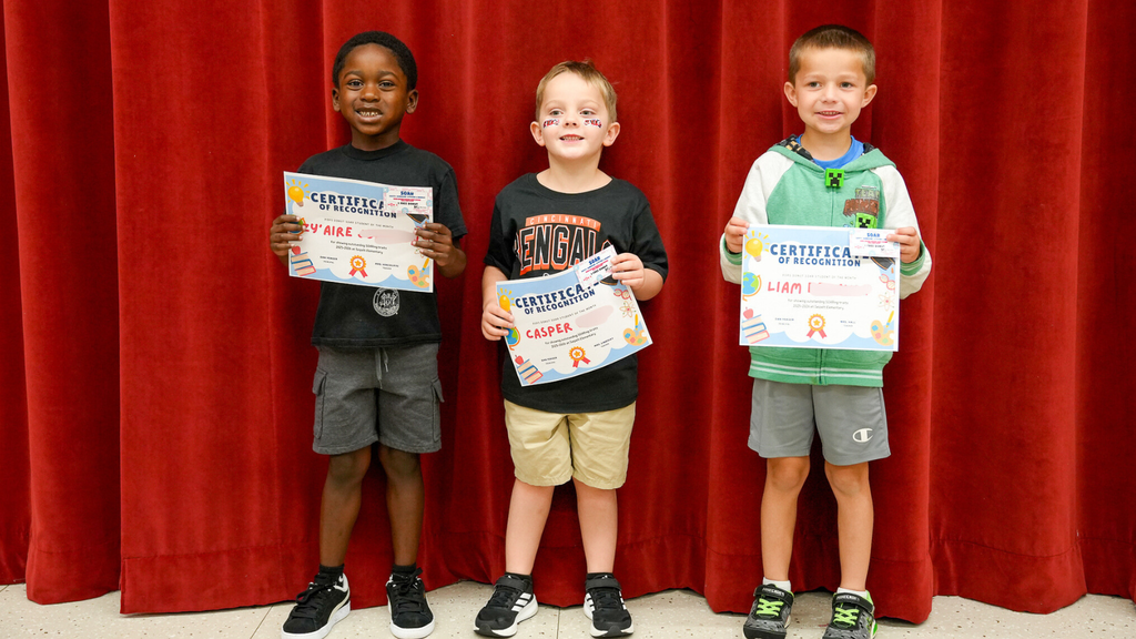 Three boys in front of a red curtain holding certificates
