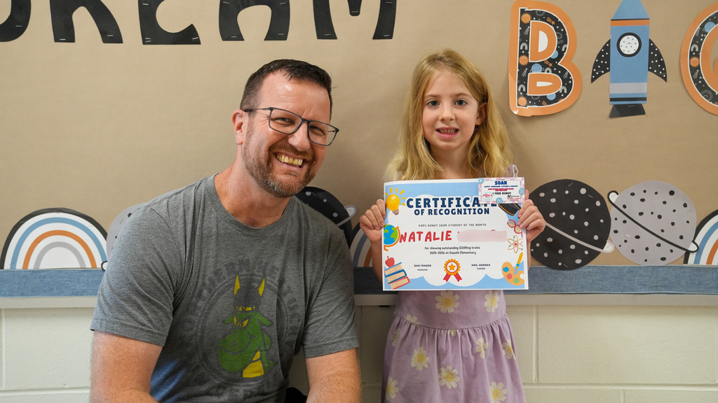 A man with glasses standing next to a girl with blonde hair holding a certificate 