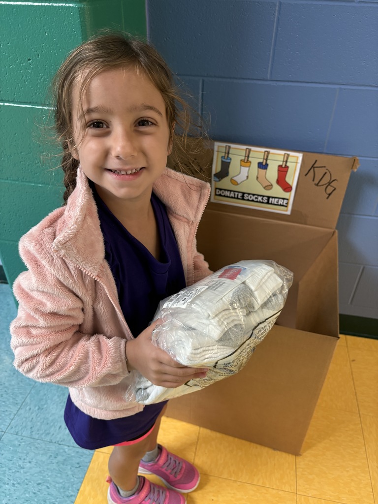 A girl in a pink jacket holding a package of white socks. 