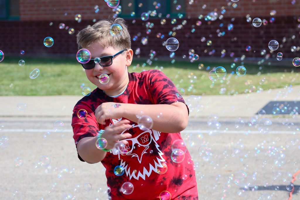 A boy with sunglasses waiving off bubbles