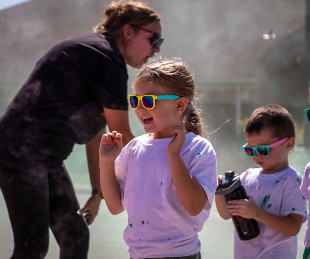 a little girl in a pink shirt with yellow sunglasses