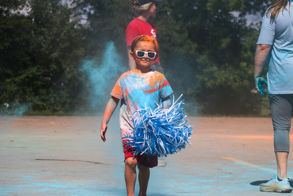 a boy covered in blue and orange powder walking with a pom pom