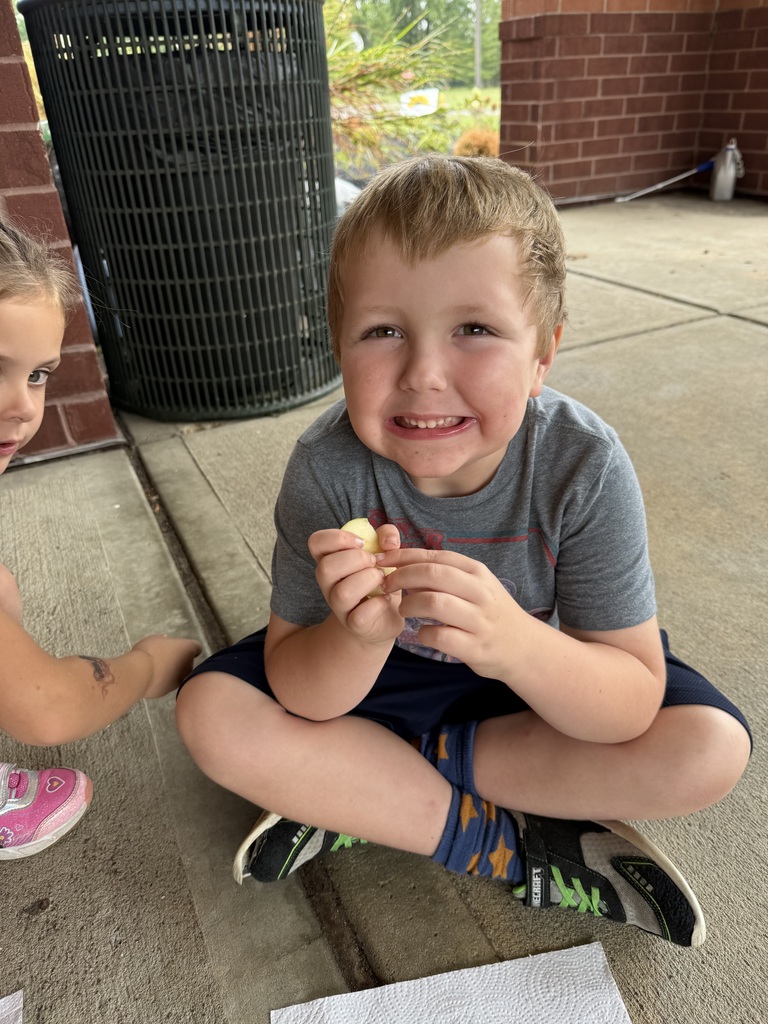 A student sitting down smiling while eating an apple