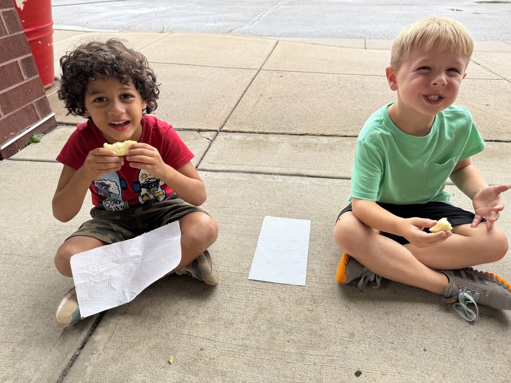 Two kids eating apples on the ground