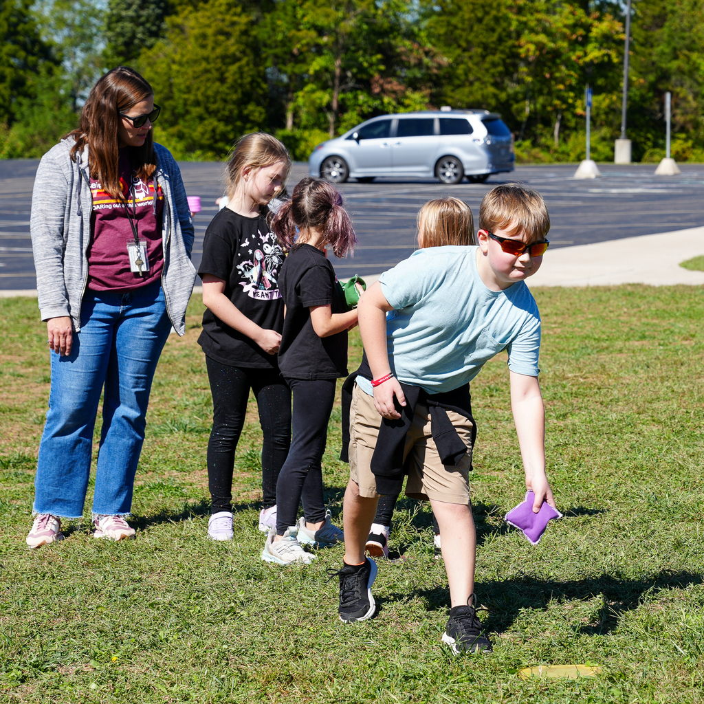 A boy wearing sunglasses playing corn hole
