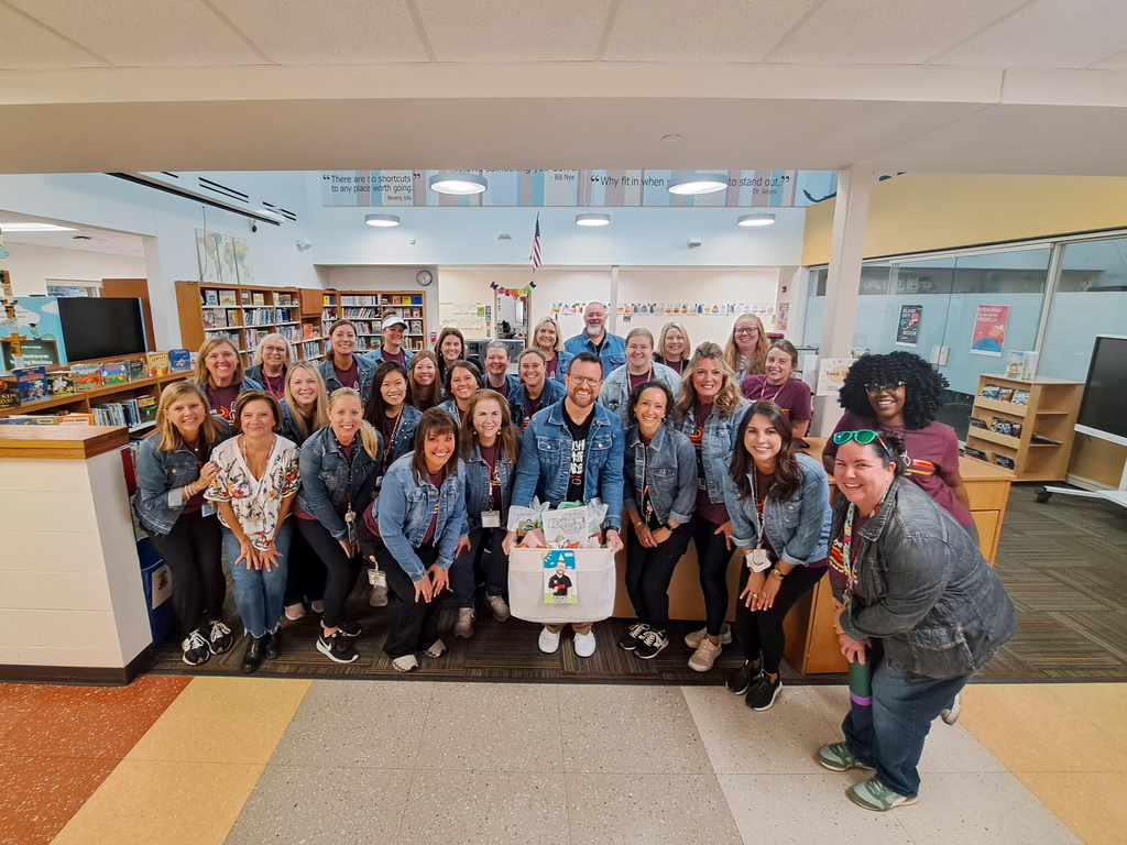 A large group photo of teachers all wearing jean jackets with a man in the center wearing one holding a box