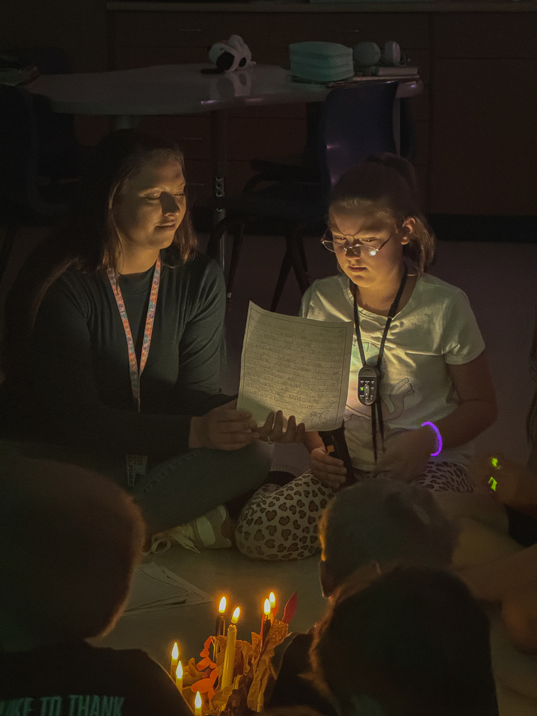 A teacher holding a piece of paper for a girl to read