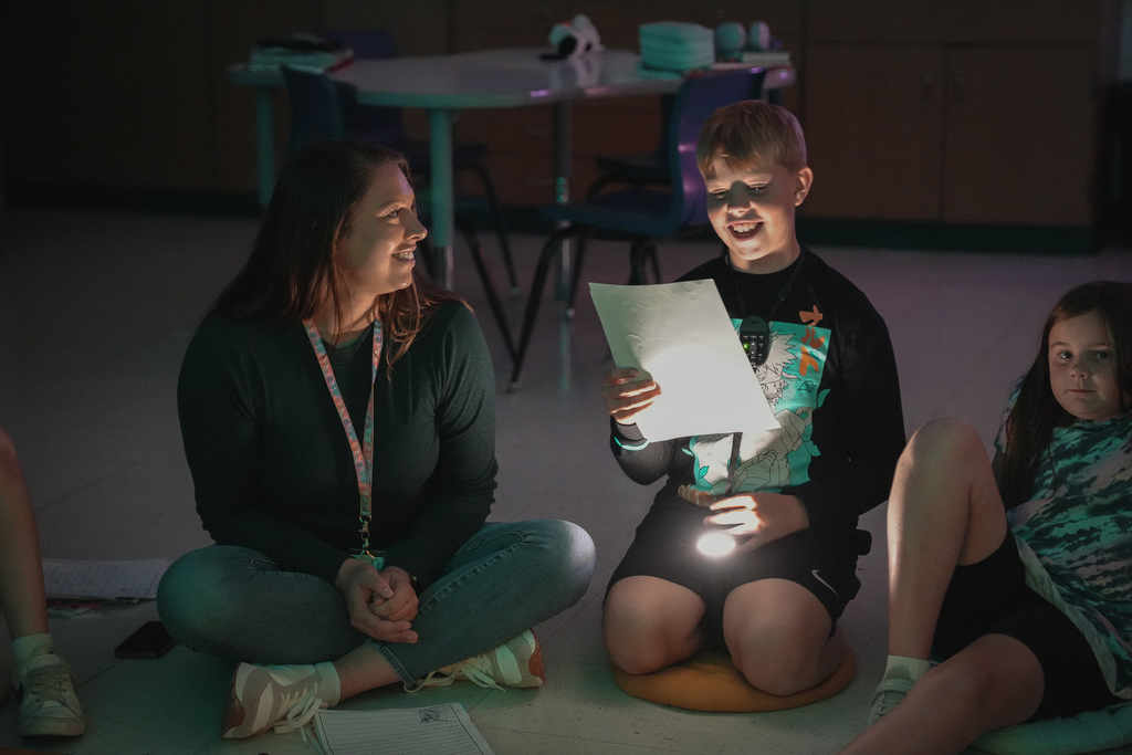 A teacher smiling at a boy reading a piece of paper
