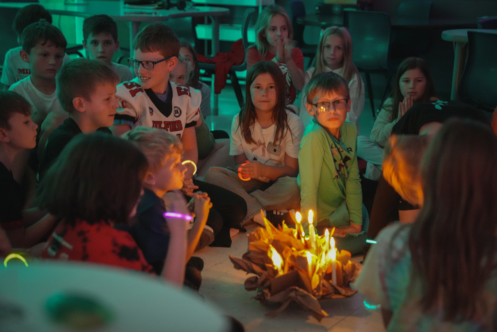 Kids sitting around listening on the floor behind a candle structure