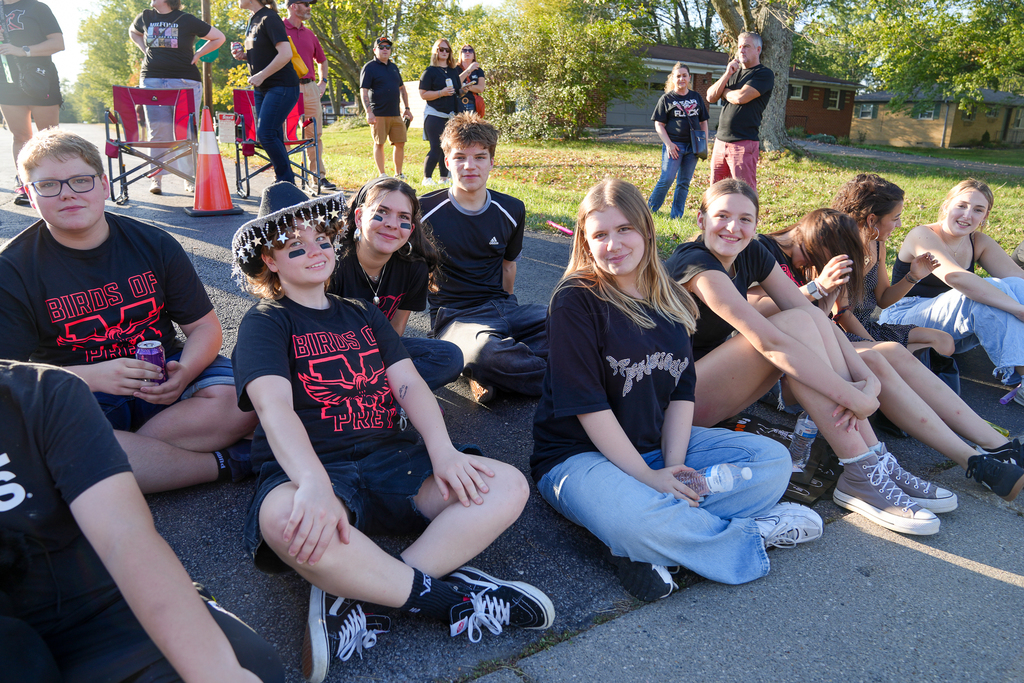 students in black sitting on the ground at a parade