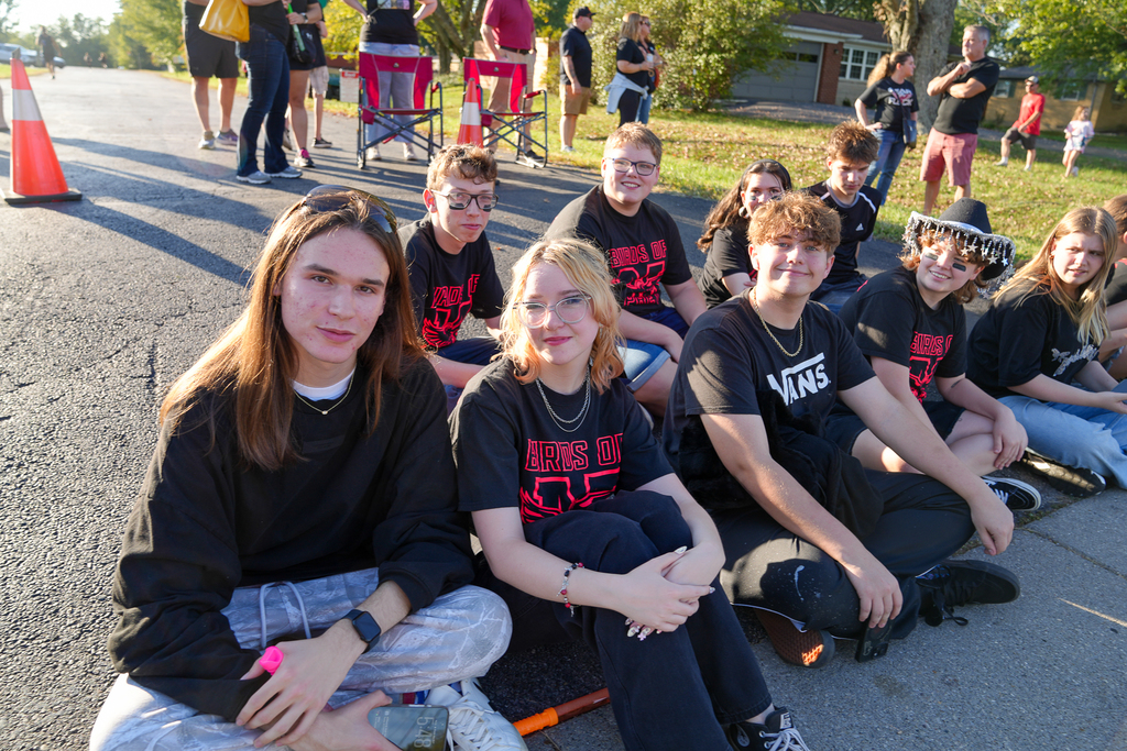 Students sitting on the ground at a parade