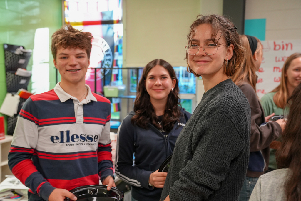 A boy with messy hair, a girl with dark brown hair and a girl with glasses smiling at the camera