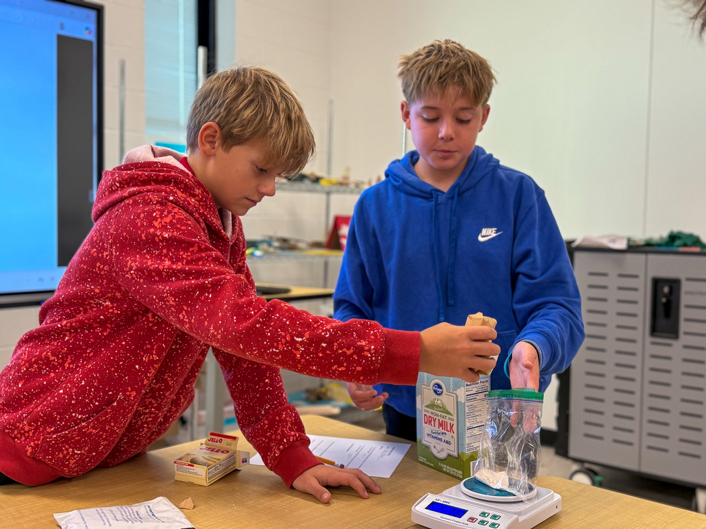 A boy in a blue hoodie helping a boy in a red hoodie measure