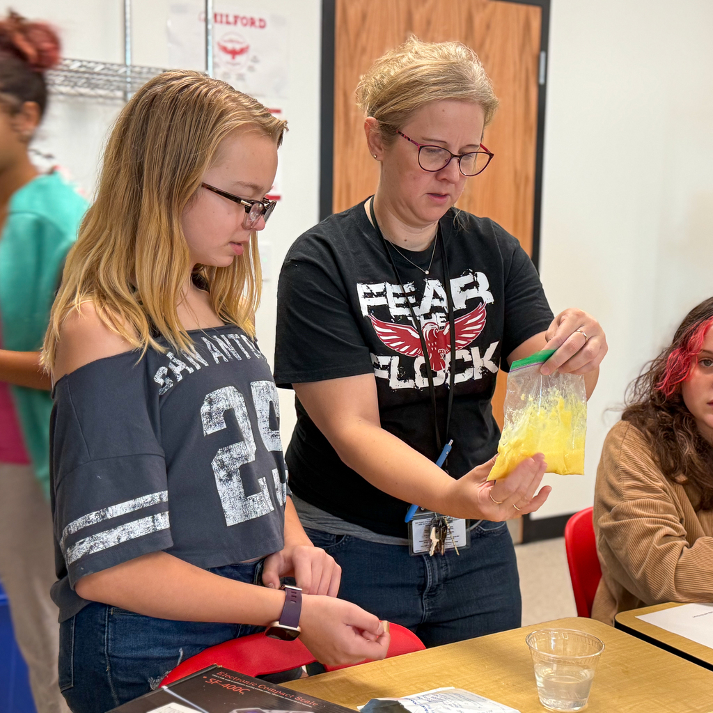 A teacher in glasses looking at a bag of yellow goop next to a girl with glasses