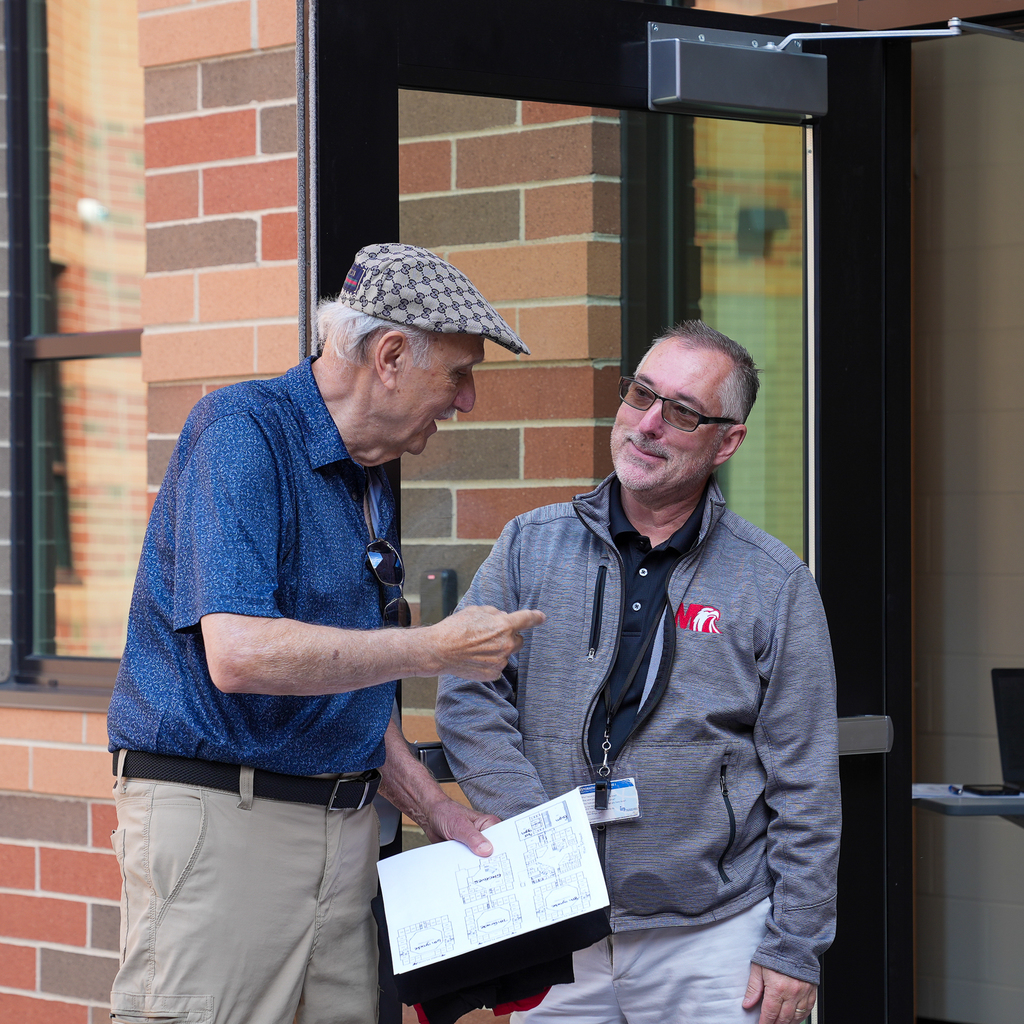 man with a flat cap talking to a man in glasses