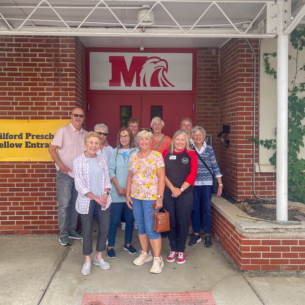 A group of seniors in front of a red door and milford logo