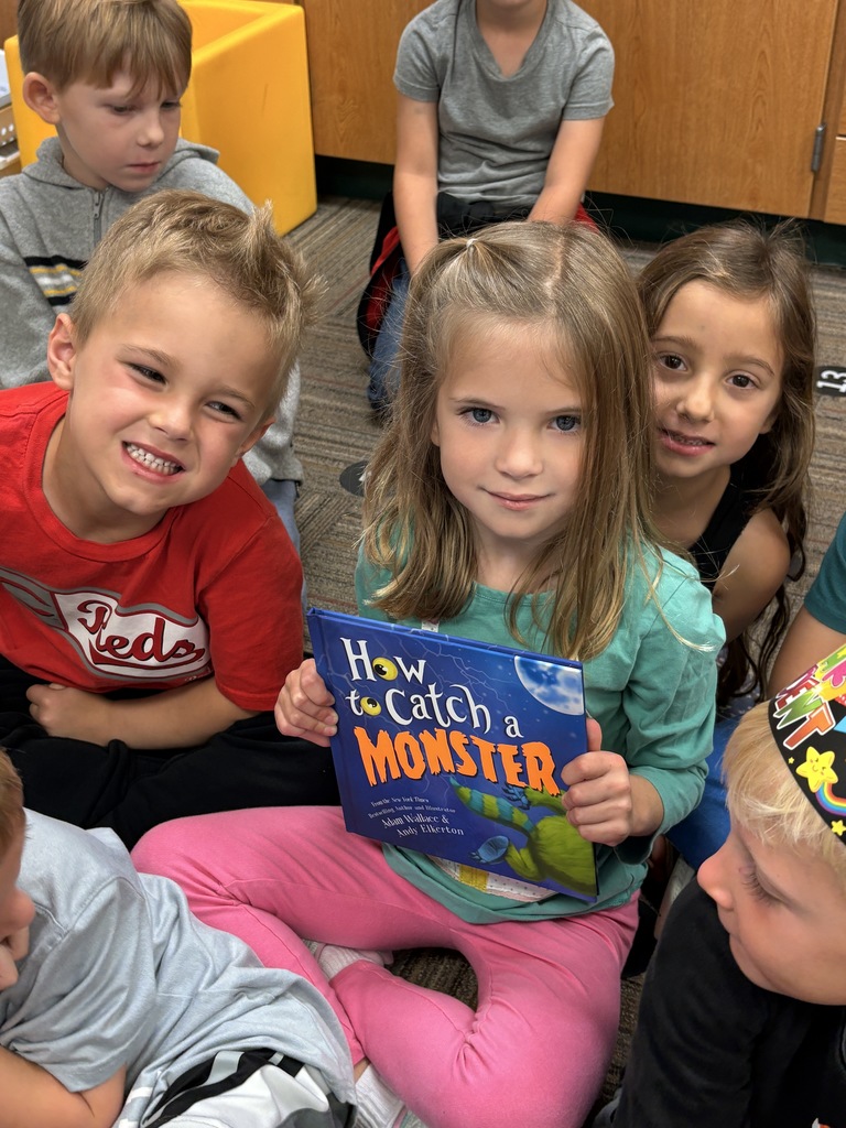 a girl holding a "how to catch a monster" book with two other kindergarteners next to her