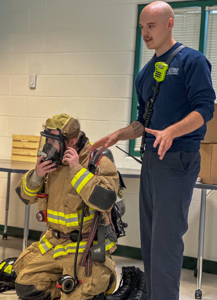 A bald man next to a firefighter getting dressed