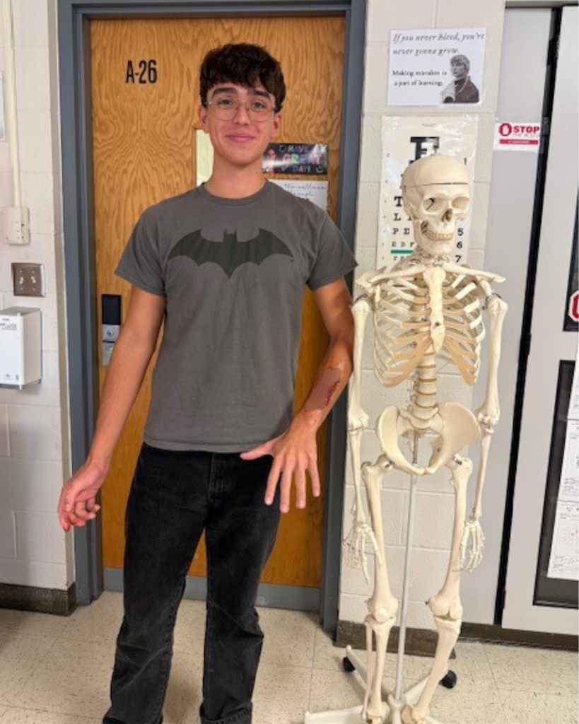 student in a batman shirt next to a skeleton