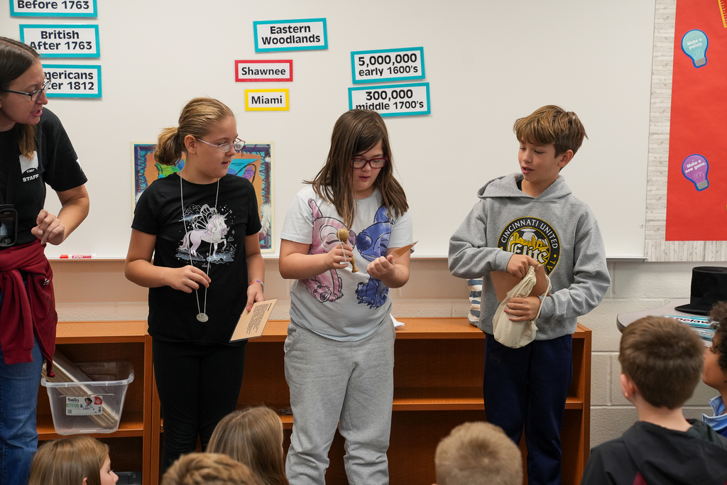 Three kids standing in front of the classroom holding relics