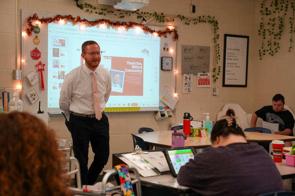 a man with glasses and a pink tie presenting to the class