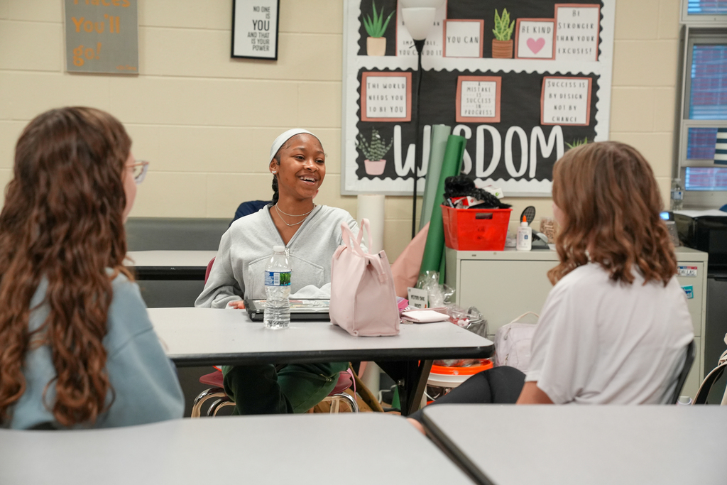 A student sitting down smiling while talking to another student 