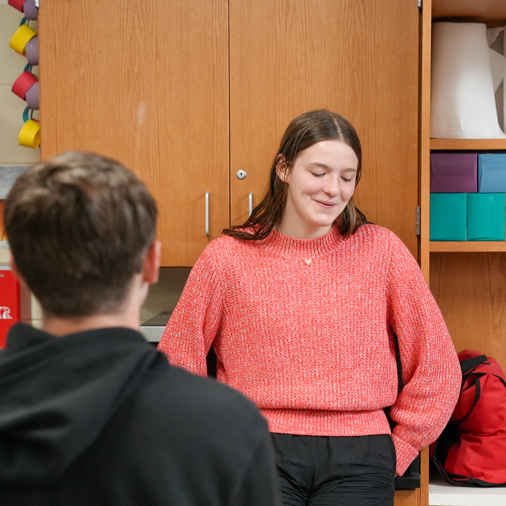 A girl wearing a pink sweater smiling at the floor 