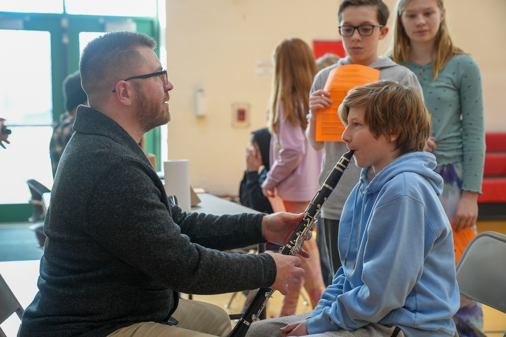A man in glasses helping a boy playing a clarinet. 