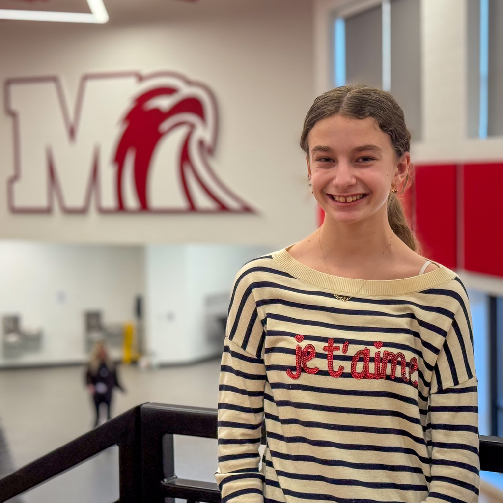 Girl in a french shirt standing in front of the Milford Logo M