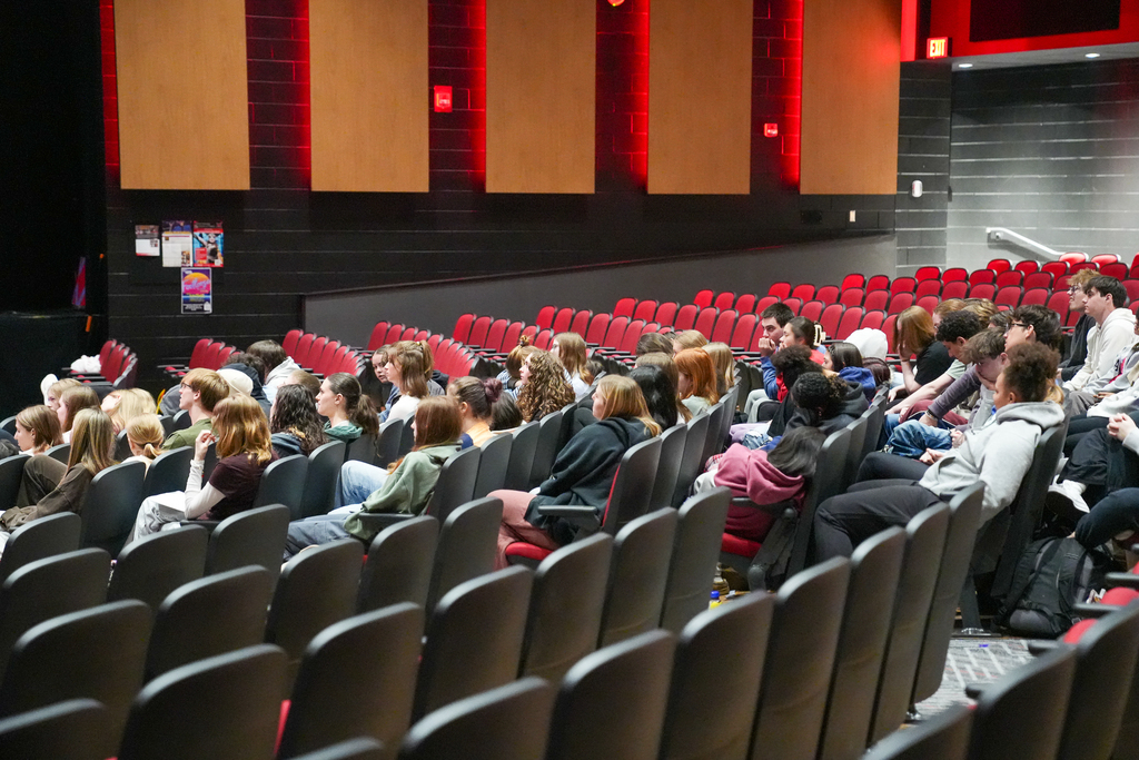 Milford High School students seated in an auditorium watch a live medical presentation streamed on a large screen as part of a learning experience for Honors Anatomy and Physiology and AP Biology.