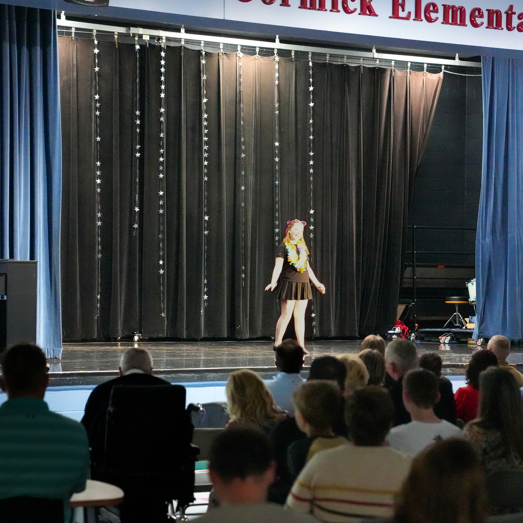 A student stands center stage performing in front of an audience at McCormick Elementary’s talent show, with a curtain backdrop decorated with hanging star lights.