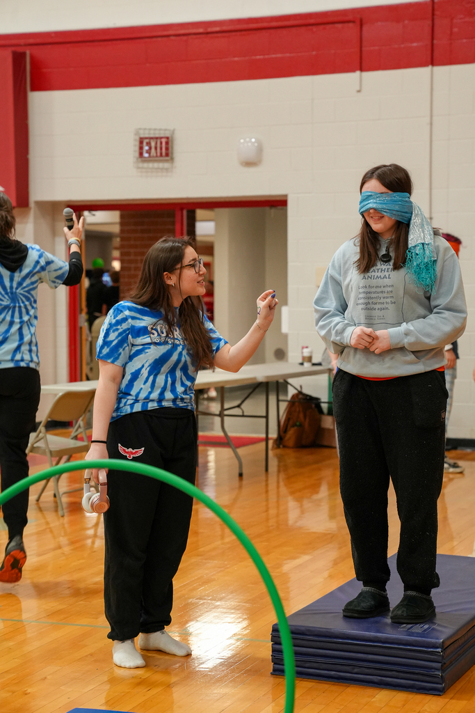One student stands on stacked mats while blindfolded as another student guides them through an activity in the gym.