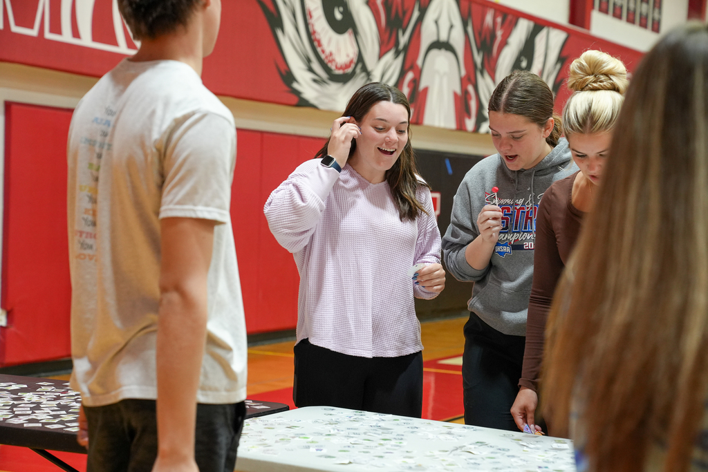 Several students stand around a table covered with cards, reacting with excitement as they participate in a group game.