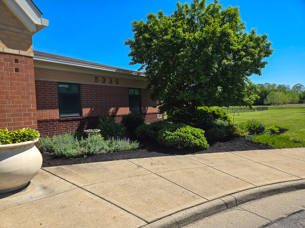 The exterior of a brick school building with the number “5330” visible above the windows, bordered by a sidewalk and newly mulched landscaping with shrubs and greenery.