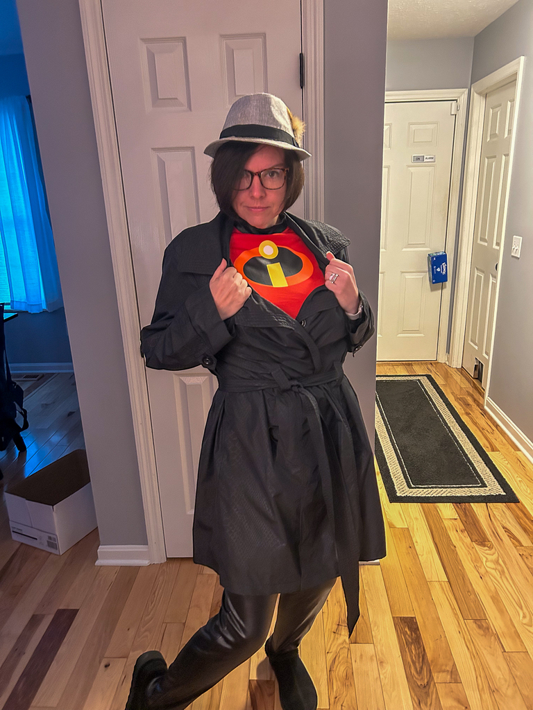 A staff member dressed as a superhero-inspired secret agent poses in a trench coat and fedora while revealing an “Incredibles” shirt underneath.